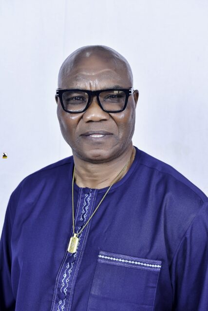 Man in dark blue clothing and glasses against a white backdrop