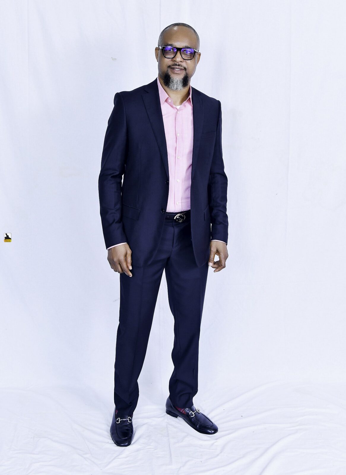 Man in a navy suit and pink shirt posing against a white backdrop