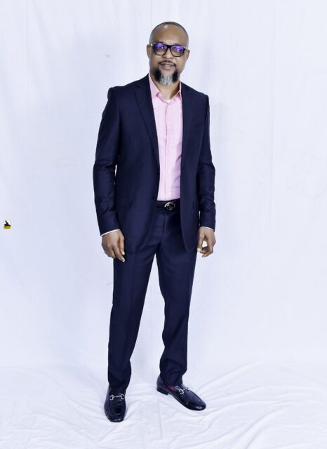 Man in a navy suit and pink shirt posing against a white backdrop