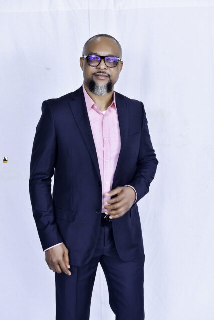 Man in a navy suit and pink shirt posing against a white backdrop