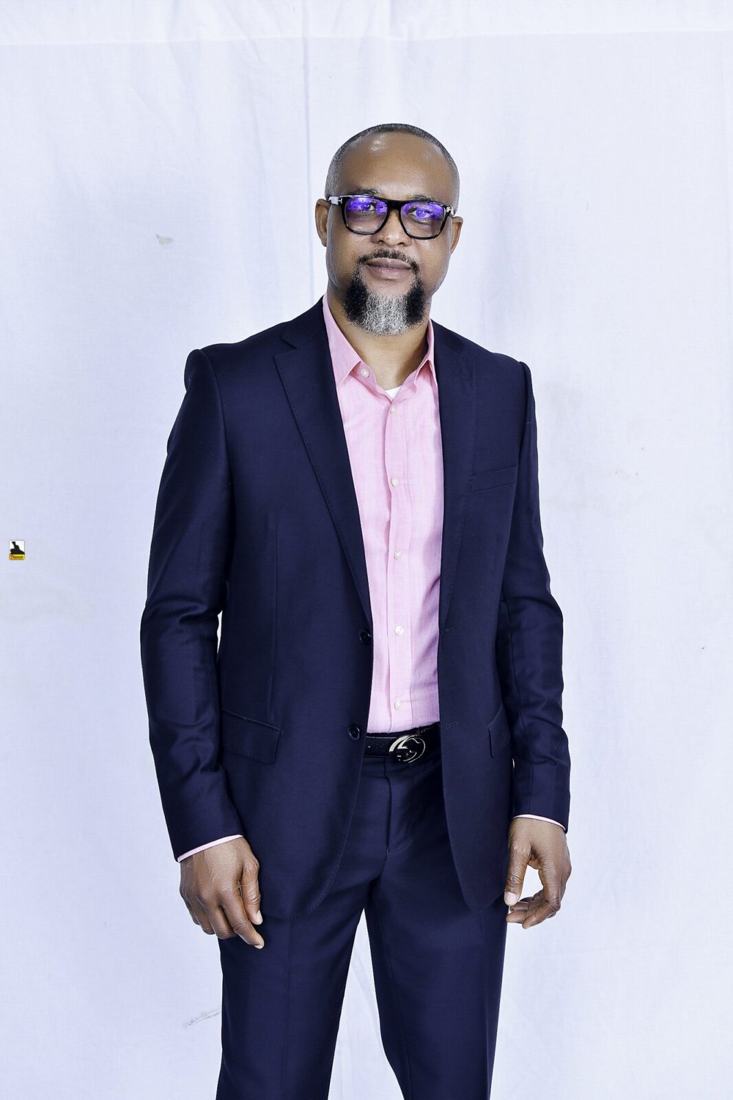 Man in a navy suit and pink shirt posing against a white backdrop