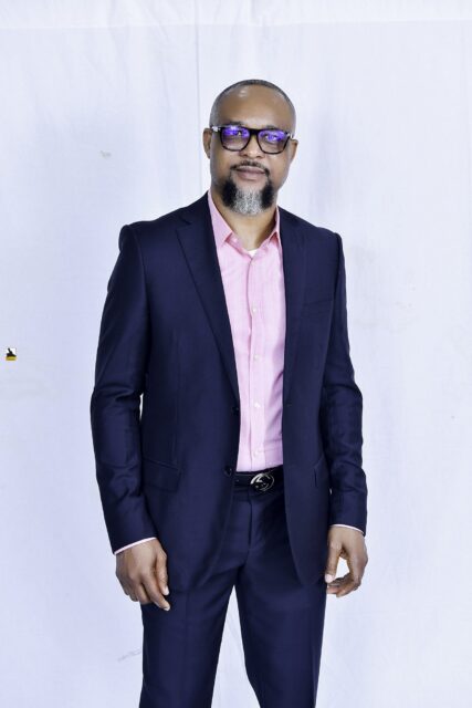 Man in a navy suit and pink shirt posing against a white backdrop