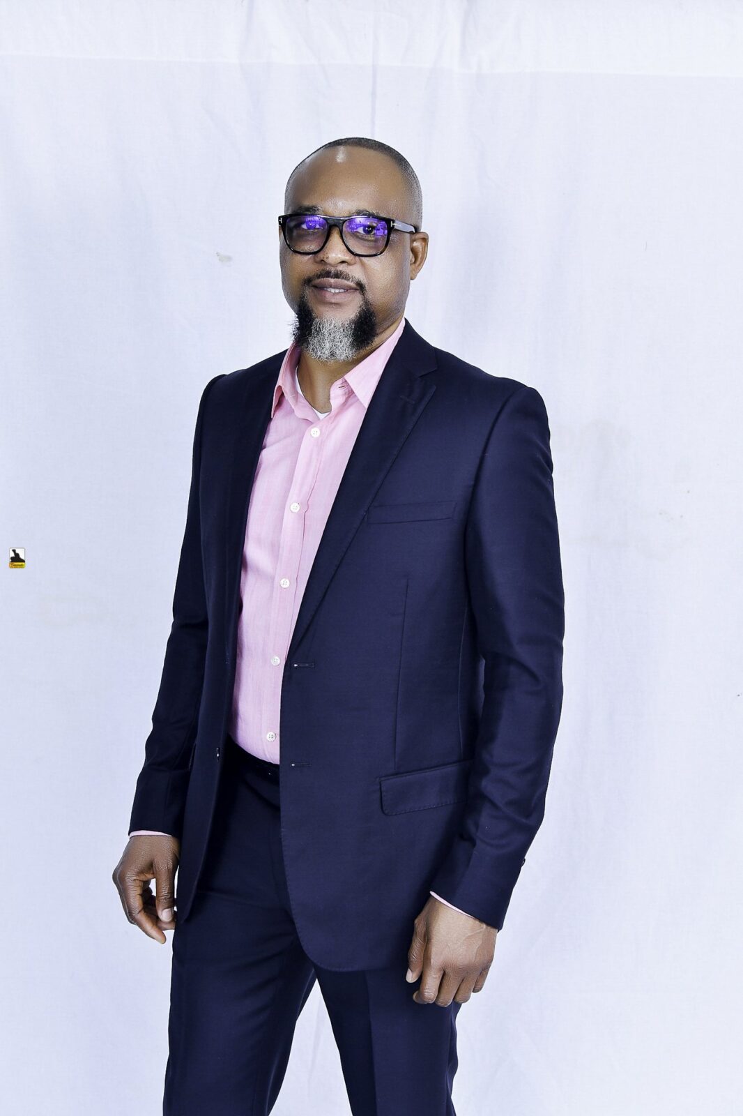 Man in a navy suit and pink shirt posing against a white backdrop