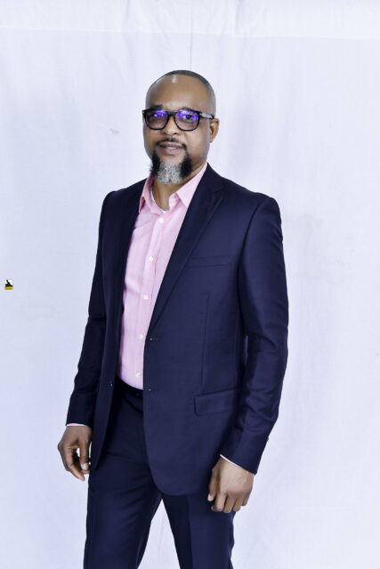 Man in a navy suit and pink shirt posing against a white backdrop