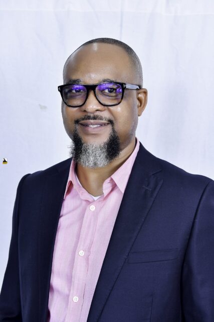 Man in a navy suit and pink shirt posing against a white backdrop