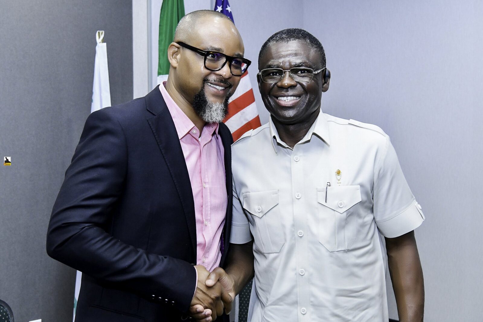 Two smiling men shaking hands beside the flags