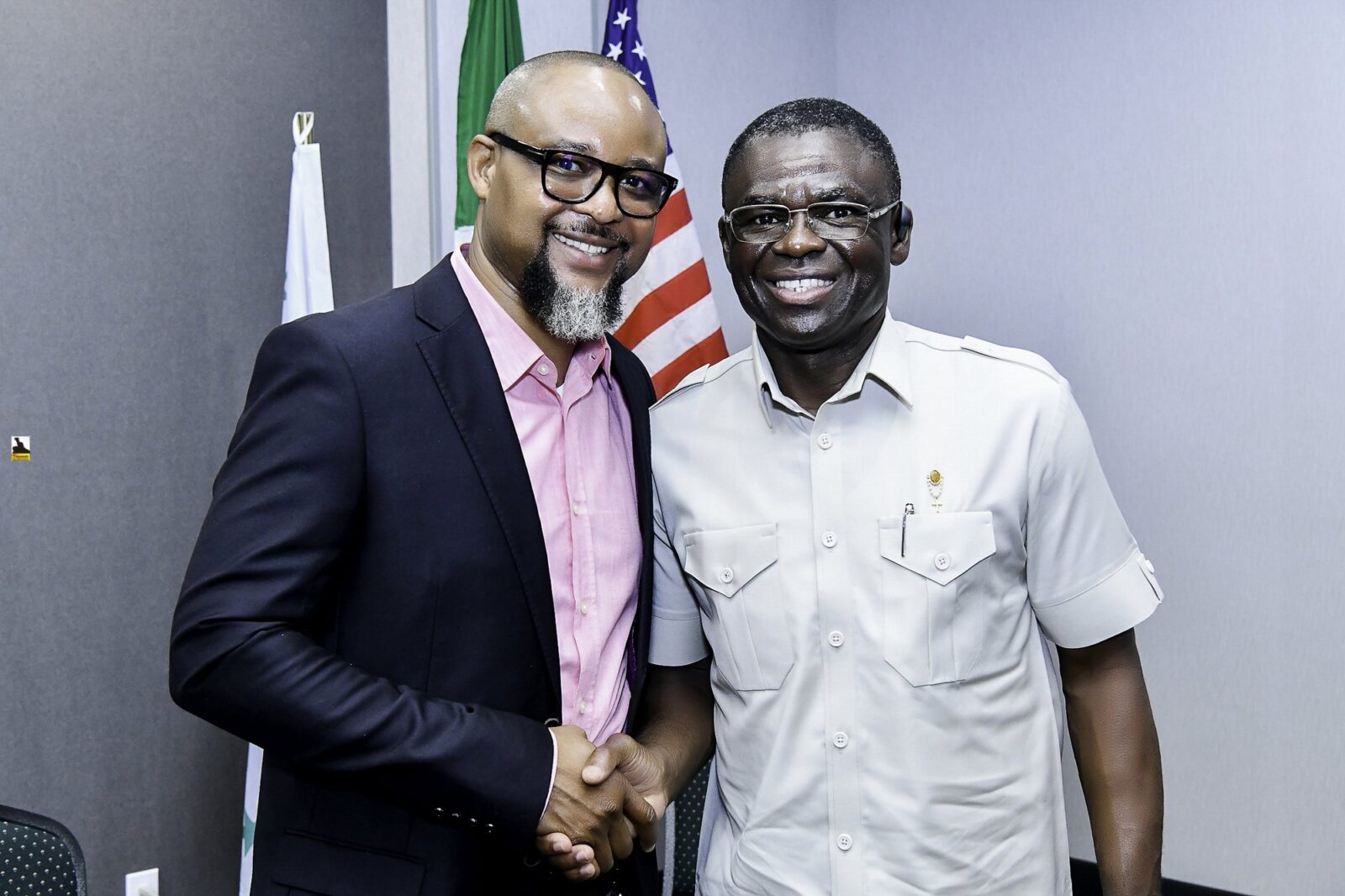 Two smiling men shaking hands beside the flags