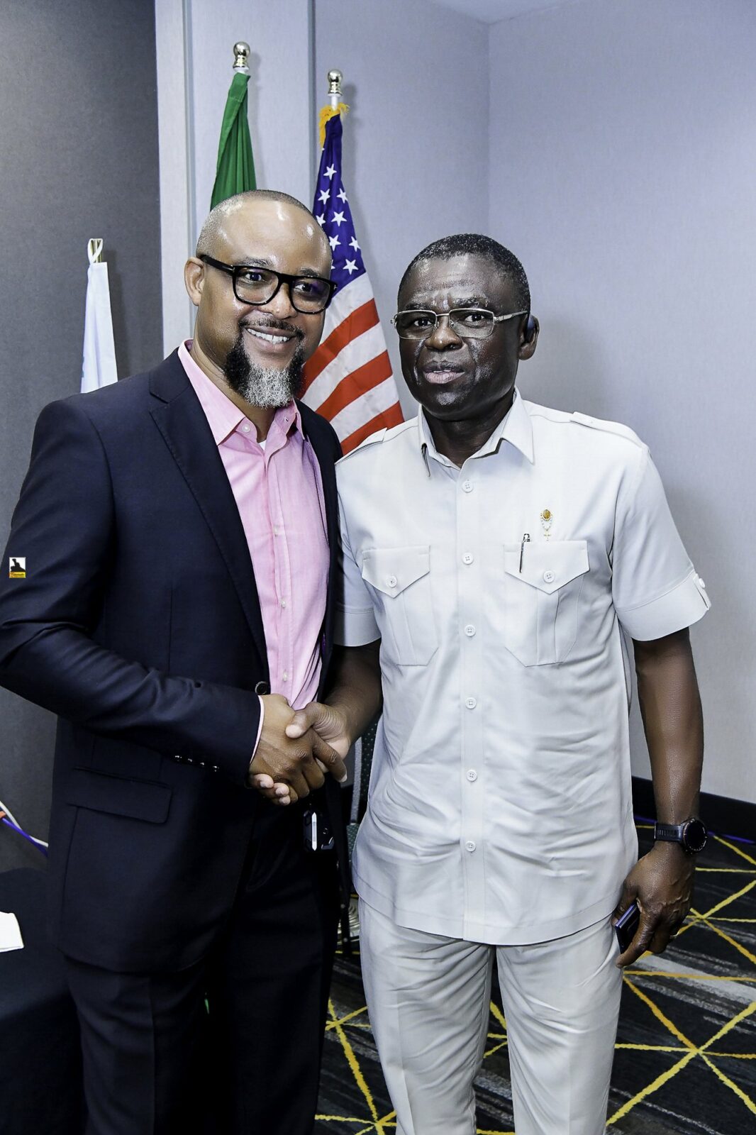 Two smiling men shaking hands beside the flags