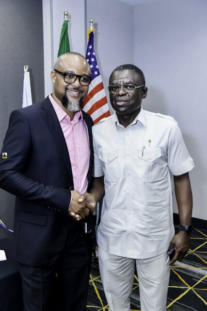 Two smiling men shaking hands beside the flags