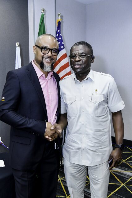Two smiling men shaking hands beside the flags