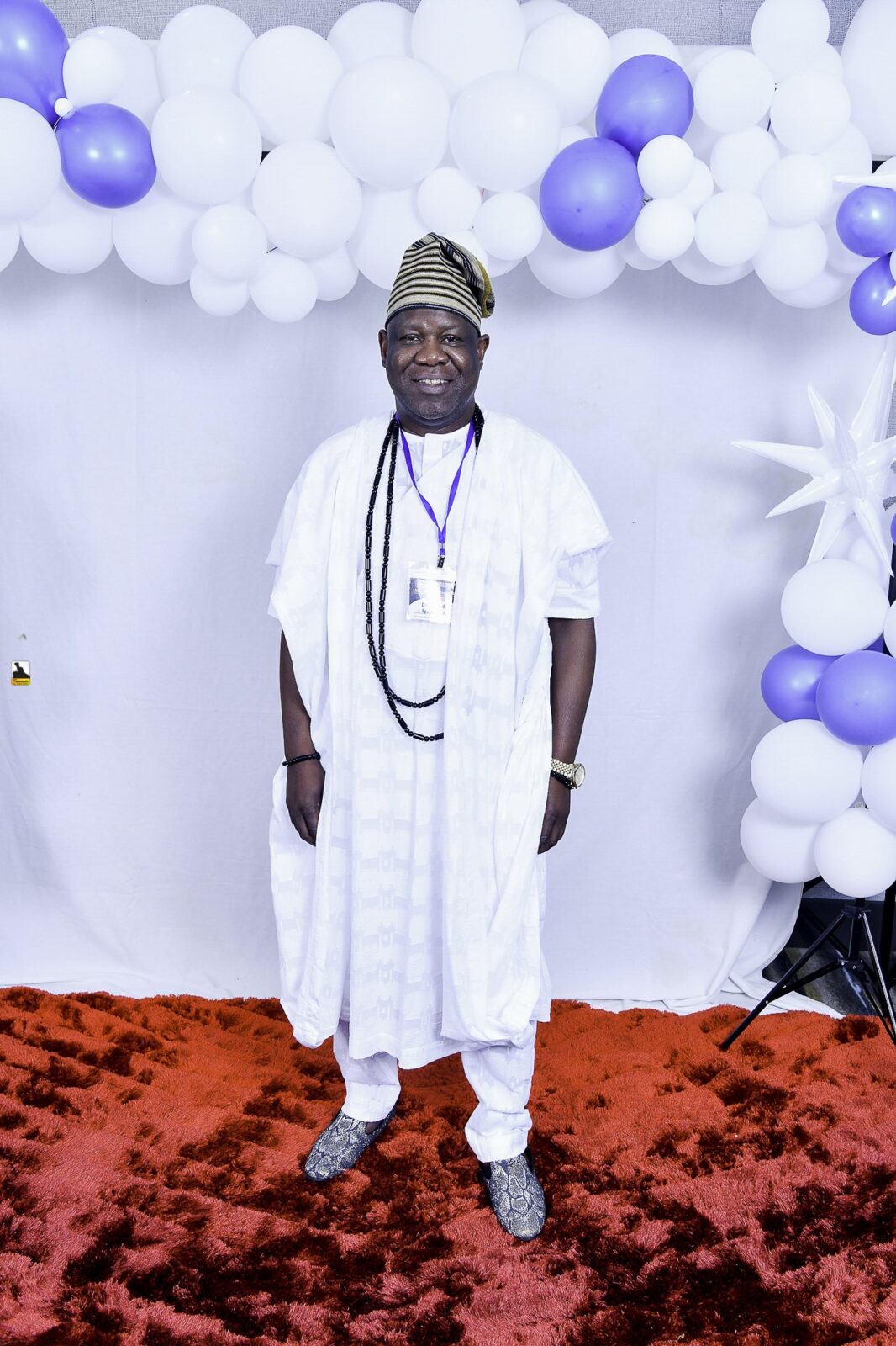 Man in white clothing with dark bead necklaces by the balloons