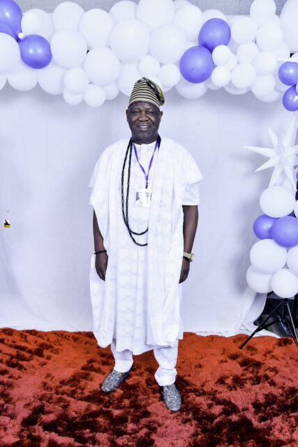 Man in white clothing with dark bead necklaces by the balloons