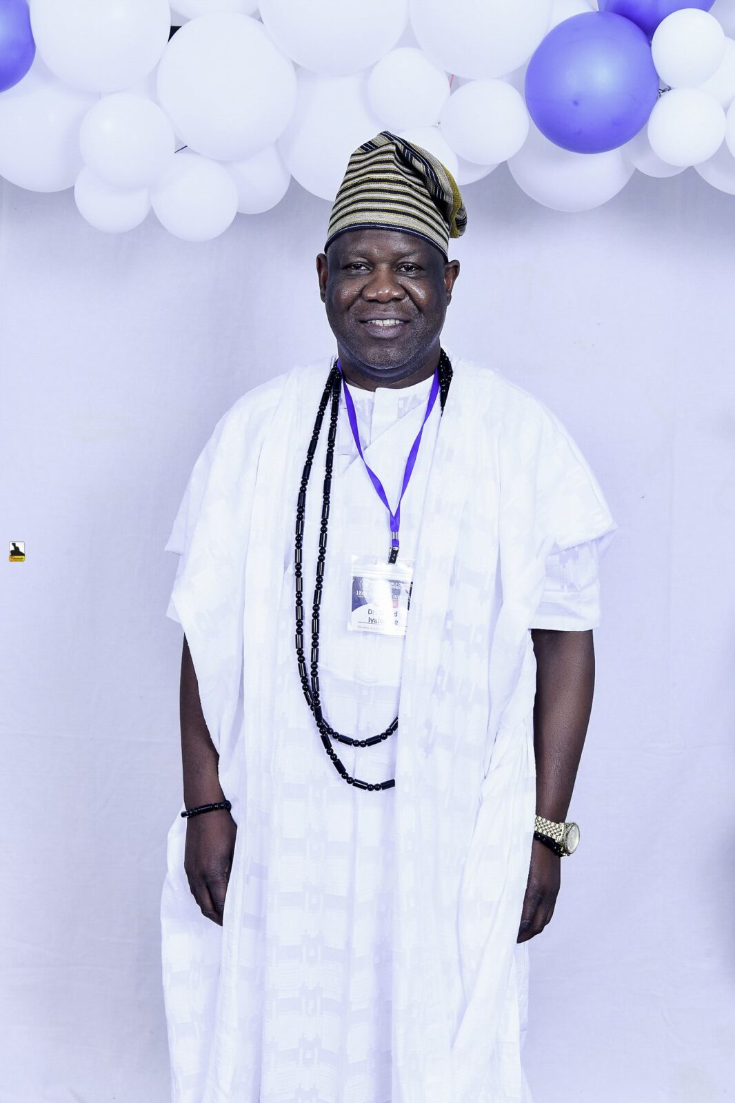 Man in white clothing with dark bead necklaces by the balloons