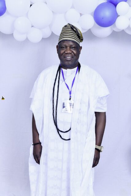 Man in white clothing with dark bead necklaces by the balloons