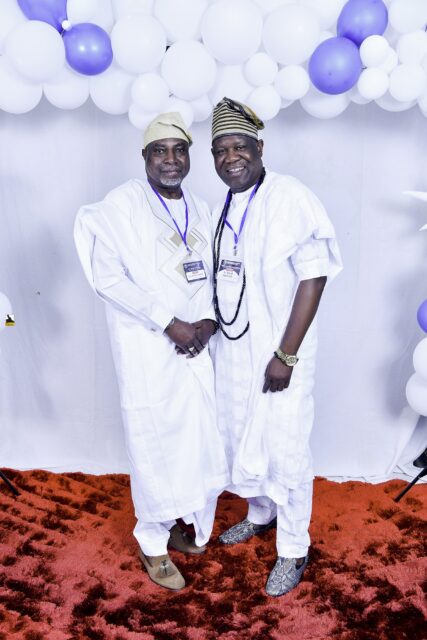 Two men in white clothing posing beside the balloon backdrop