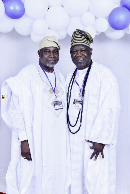 Two men in white clothing posing beside the balloon backdrop