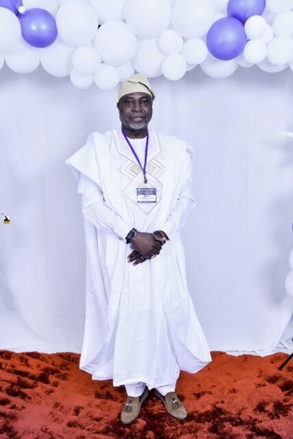 Man in embroidered white clothing and a pale cap by the balloons