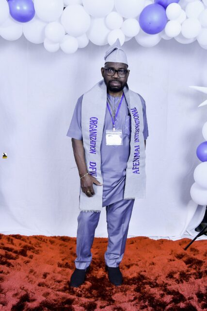Man in gray clothing, a cap and a lettered sash by the balloons