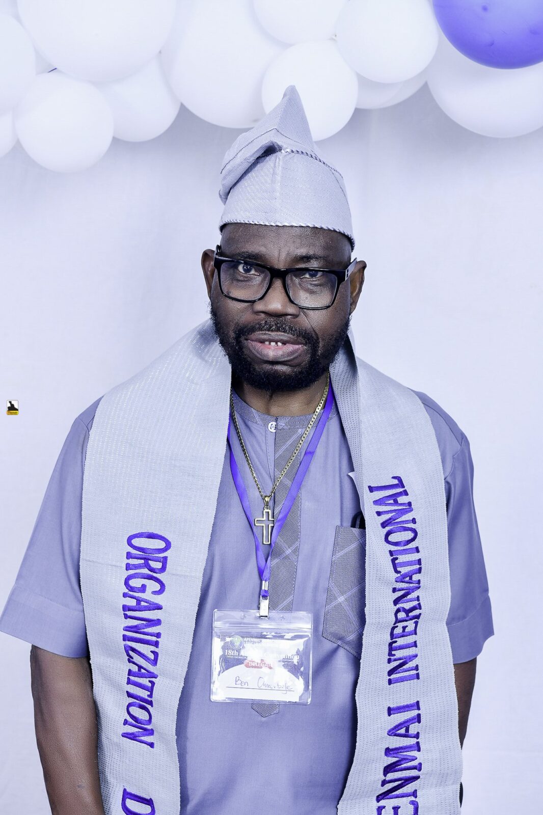 Man in gray clothing, a cap and a lettered sash by the balloons