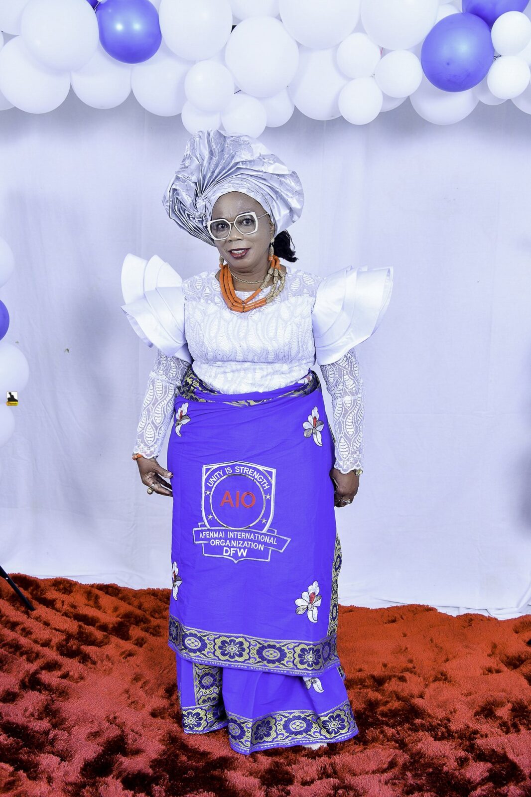 Woman in a white blouse, blue wrapper and silver headwrap by the balloons