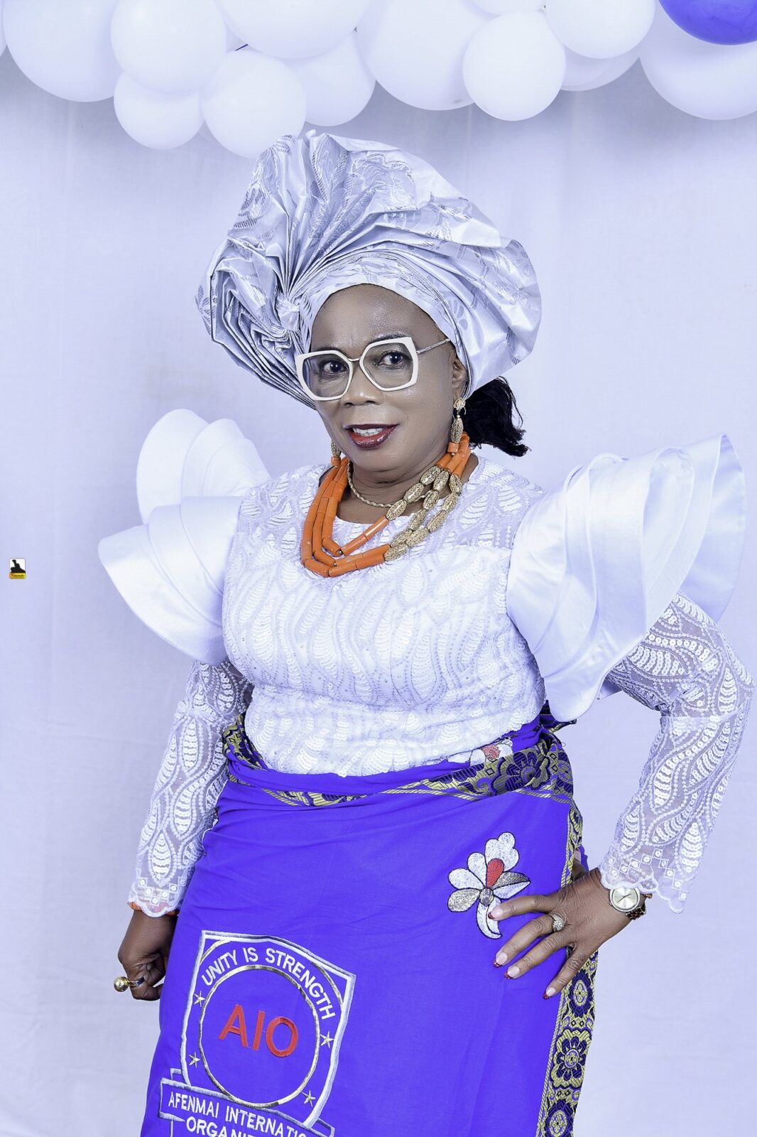 Woman in a white blouse, blue wrapper and silver headwrap by the balloons