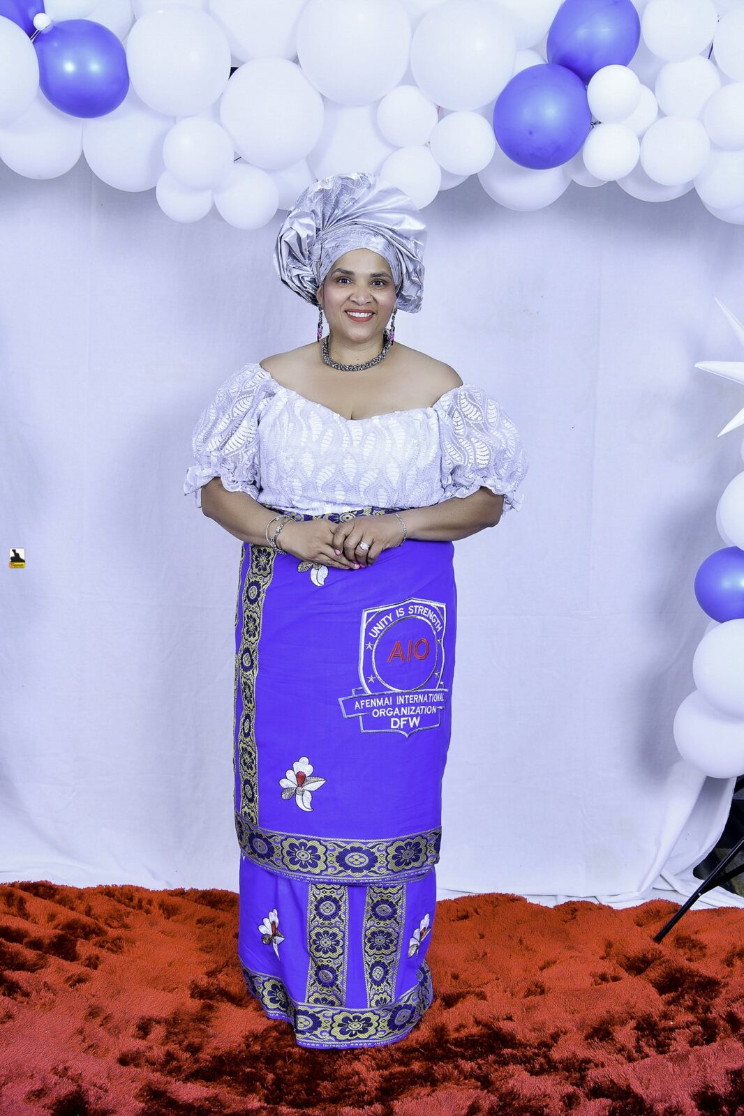 Woman in a white blouse, blue wrapper and silver headwrap by the balloons