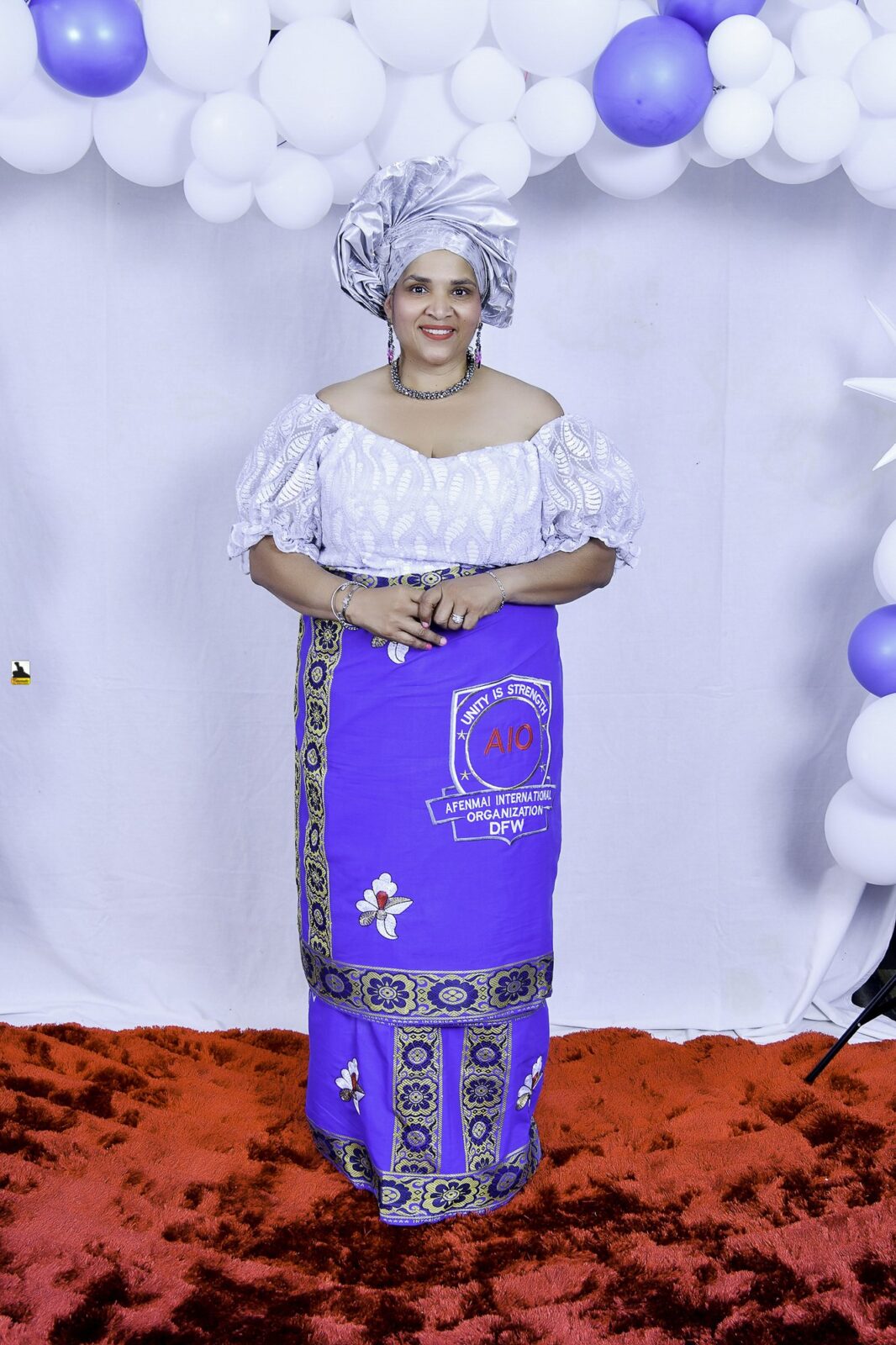 Woman in a white blouse, blue wrapper and silver headwrap by the balloons