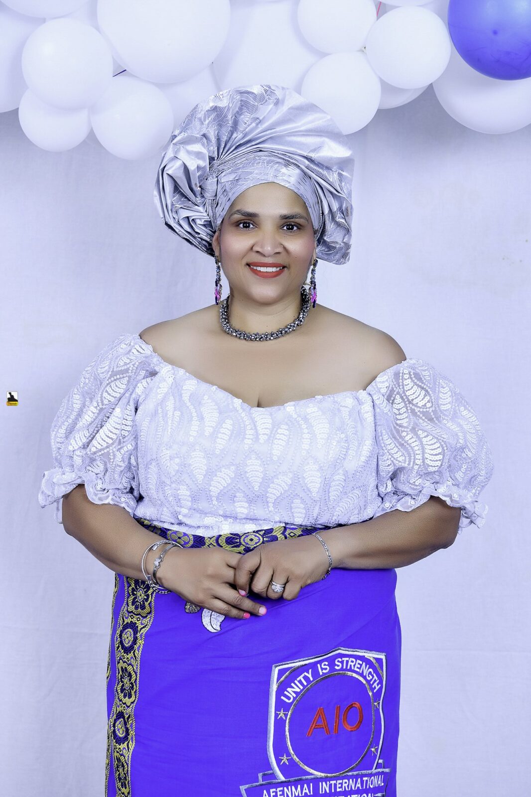 Woman in a white blouse, blue wrapper and silver headwrap by the balloons