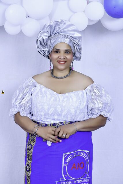 Woman in a white blouse, blue wrapper and silver headwrap by the balloons