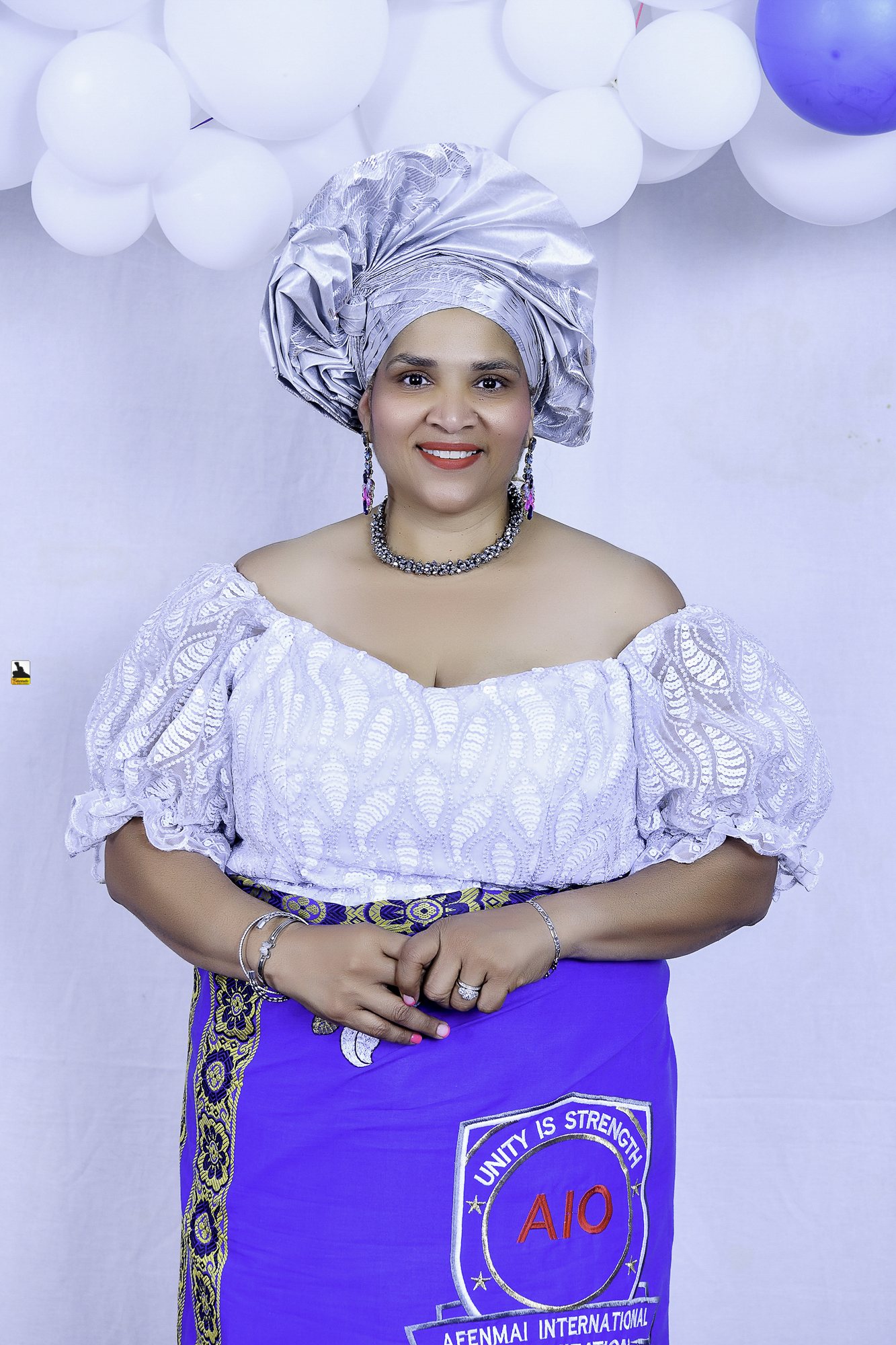 Woman in a white blouse, blue wrapper and silver headwrap by the balloons