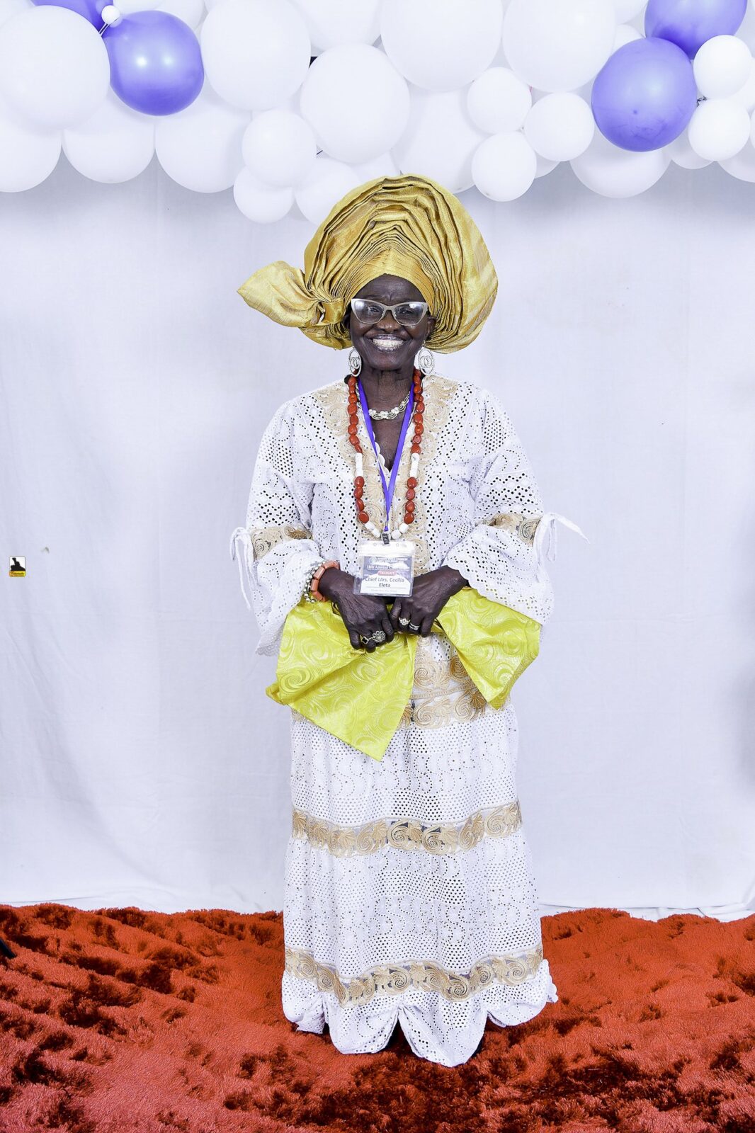Woman in white lace and a gold headwrap holding a yellow handbag