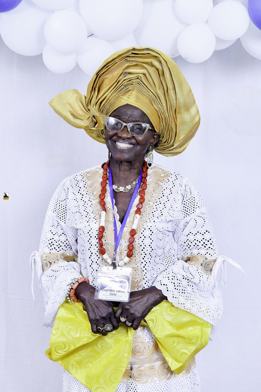 Woman in white lace and a gold headwrap holding a yellow handbag