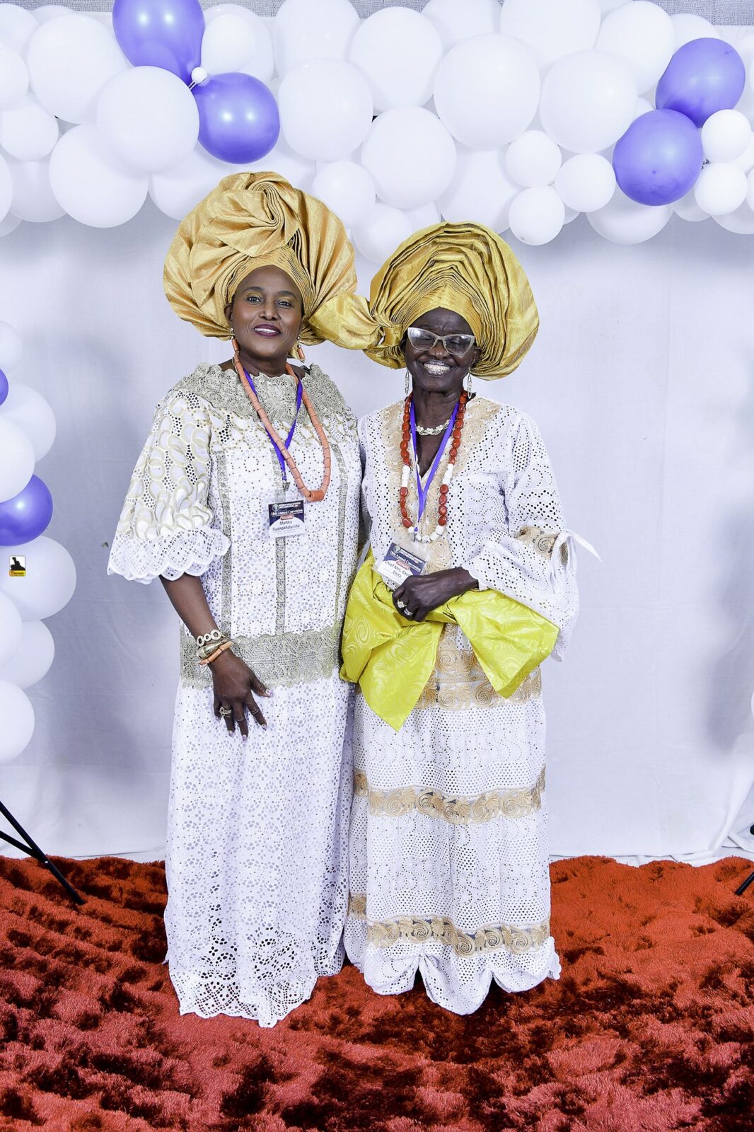 Two women in white lace and gold headwraps standing together