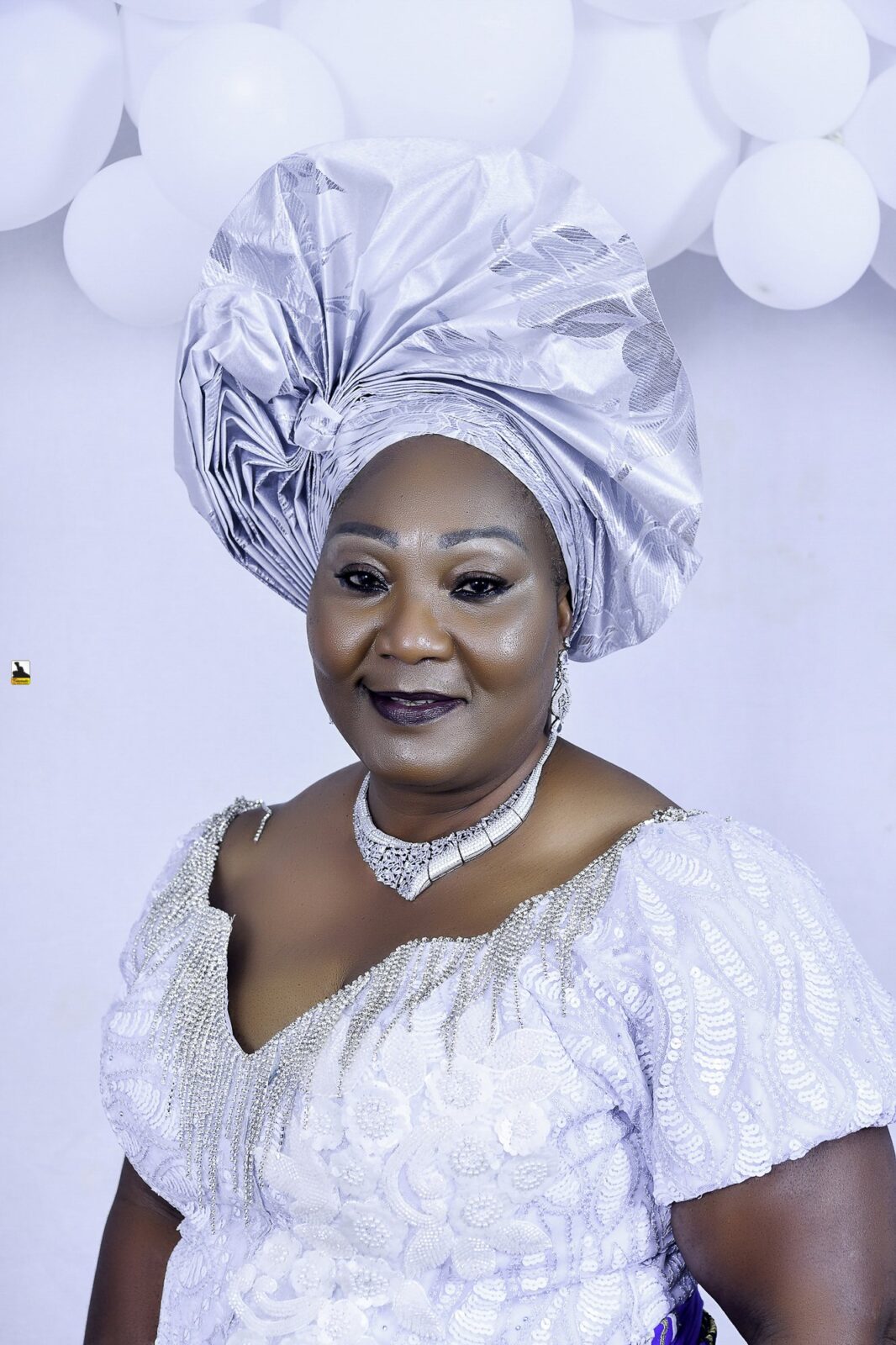 Woman in a white blouse, blue wrapper and silver headwrap posing by the balloons