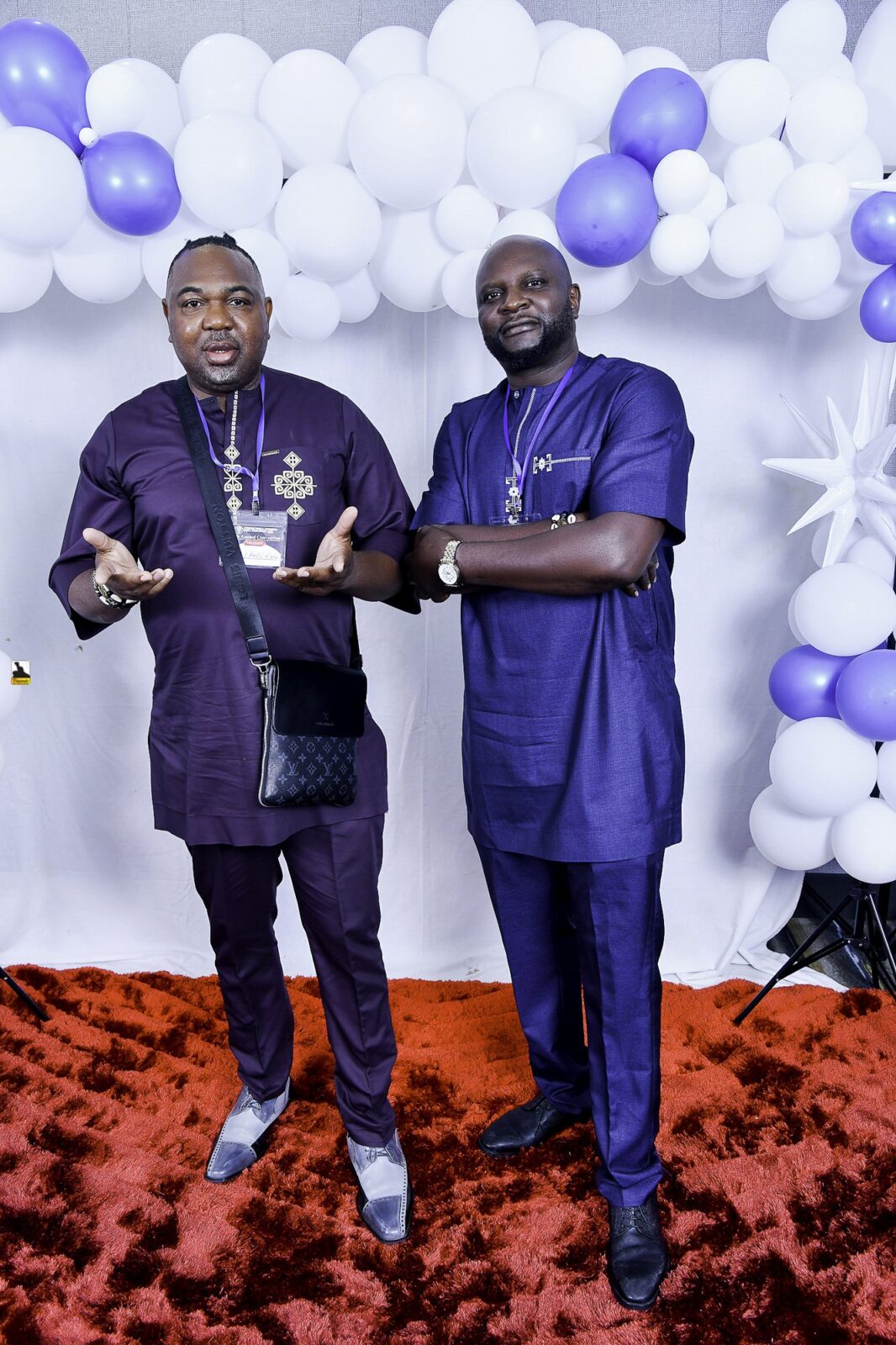 Two men in blue outfits smiling together beneath the balloons