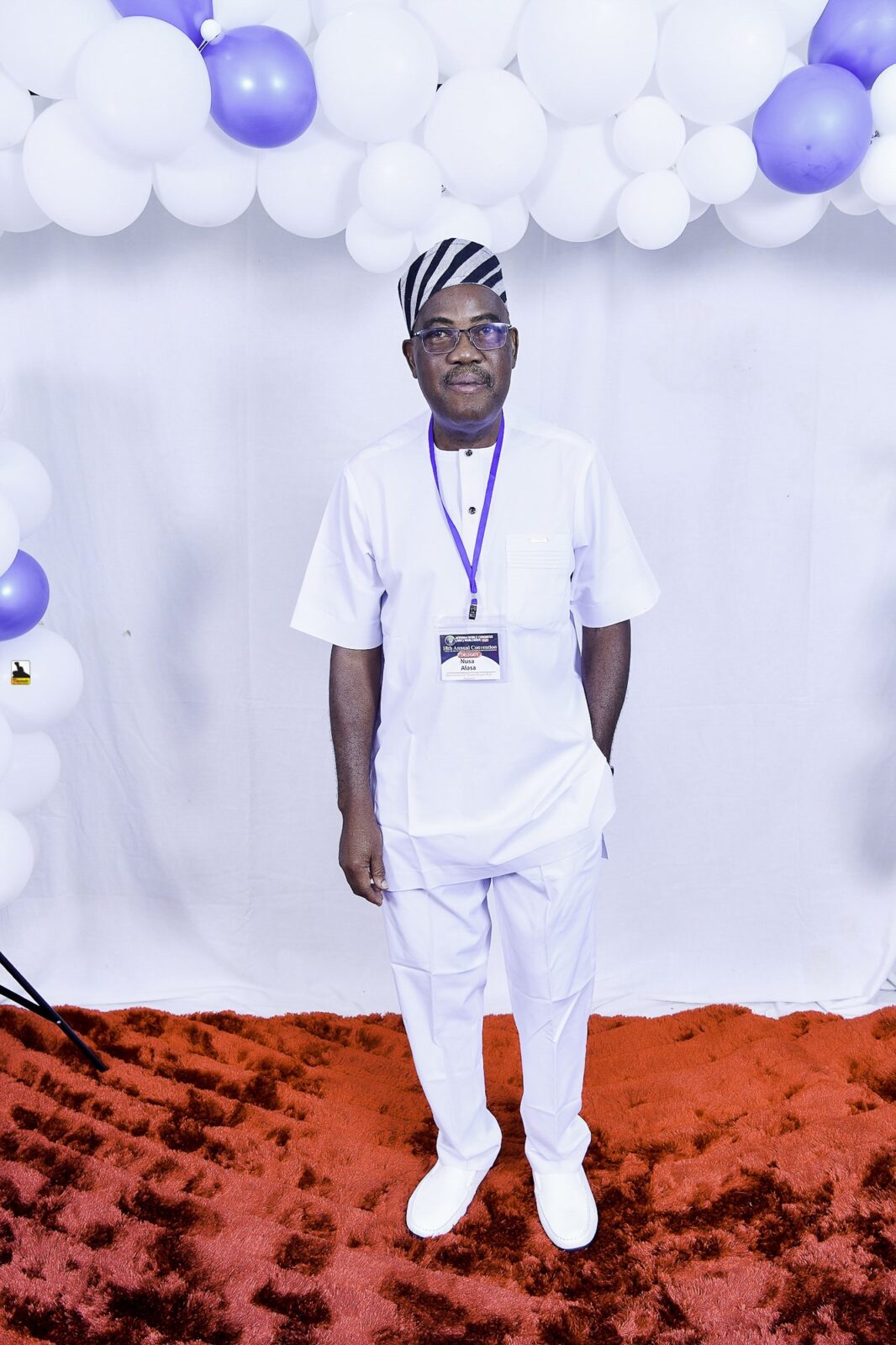 Man in white clothing and a striped cap posing by the balloons