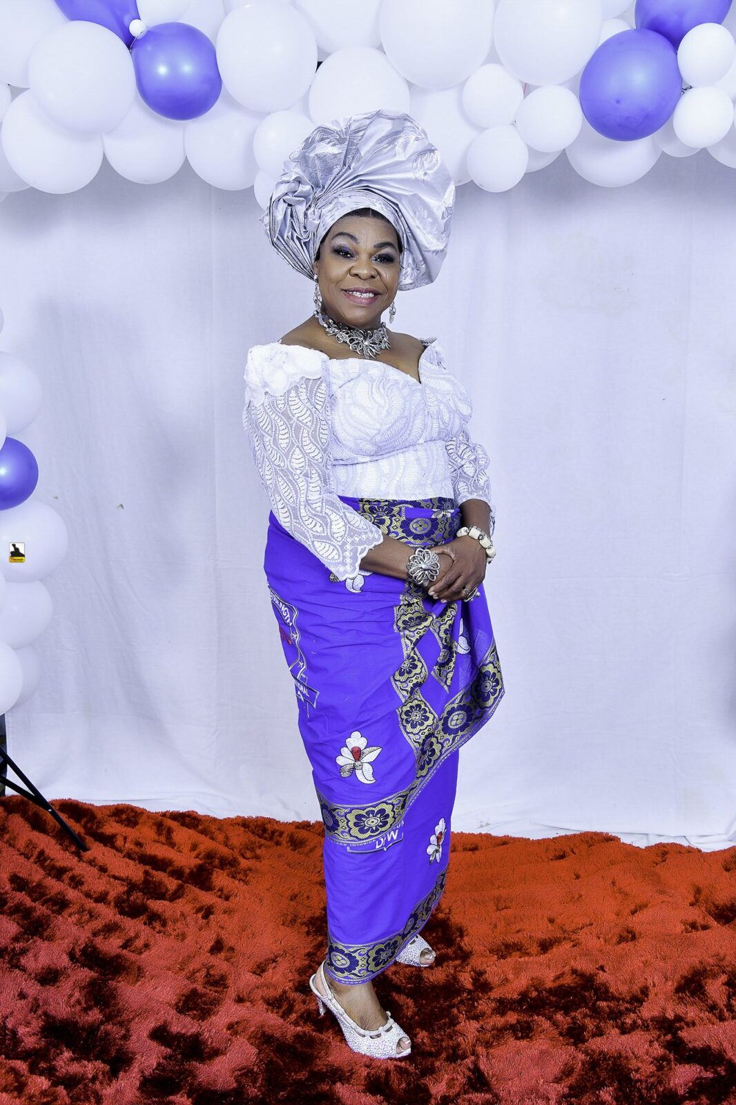 Woman in white lace, a blue wrapper and a silver headwrap by the balloons