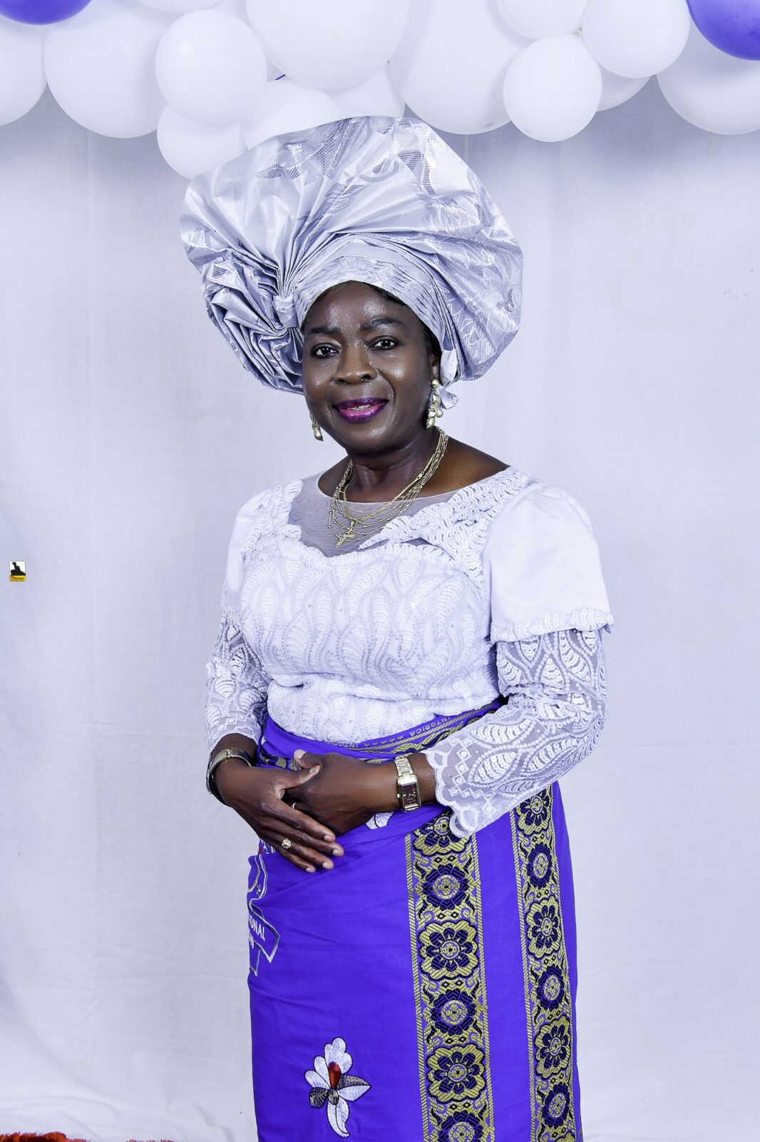 Woman in white and blue clothing and a silver headwrap by the balloons