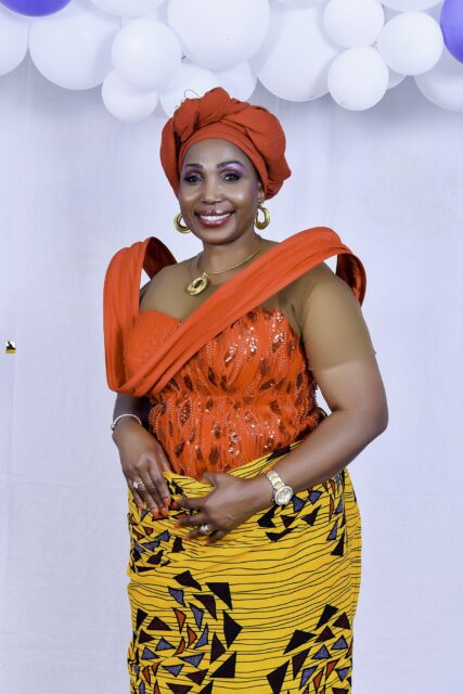 Woman in an orange top and headwrap with a yellow patterned wrapper