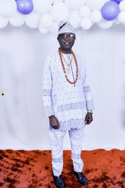 Man in white patterned clothing and bead necklaces by the balloons