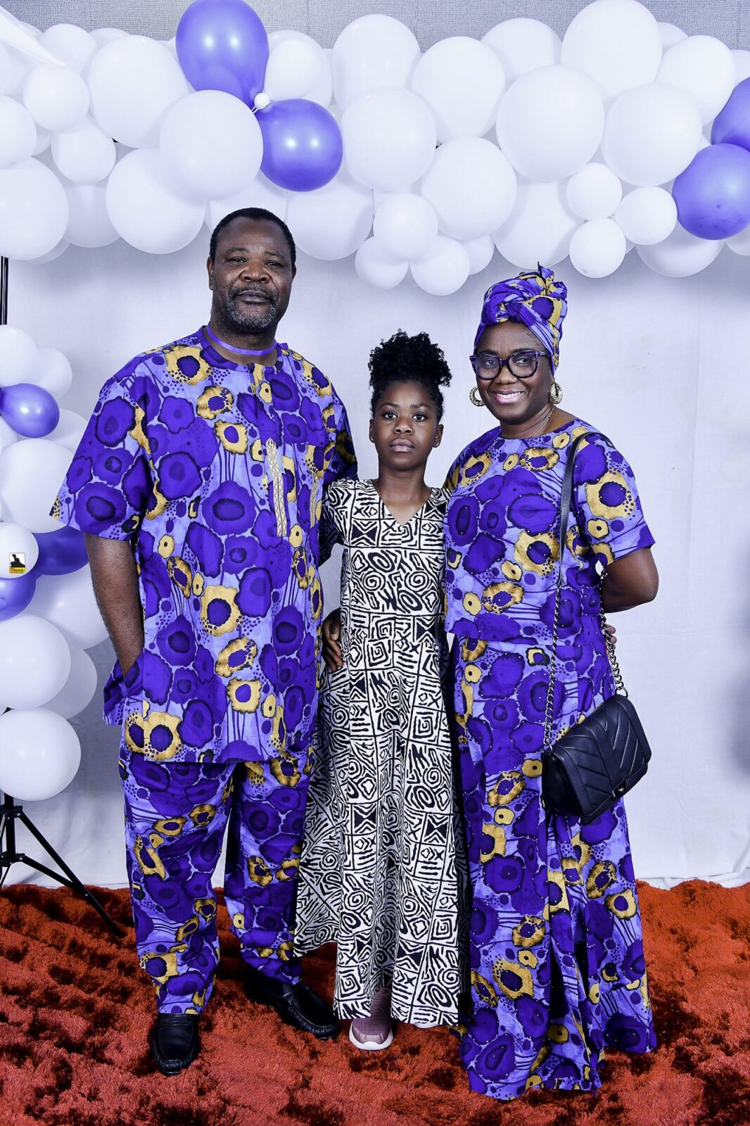 Three attendees in blue and black patterned clothing beneath the balloons