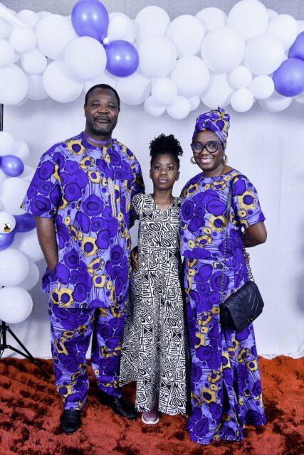 Three attendees in blue and black patterned clothing beneath the balloons