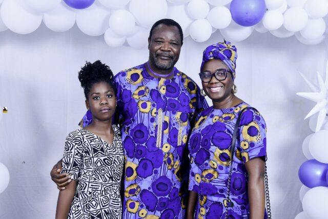 Three attendees in blue and black patterned clothing beneath the balloons