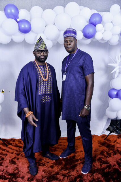 Two men in dark blue clothing and caps posing together