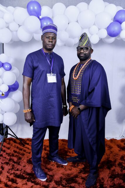 Two men in dark blue clothing and caps posing together