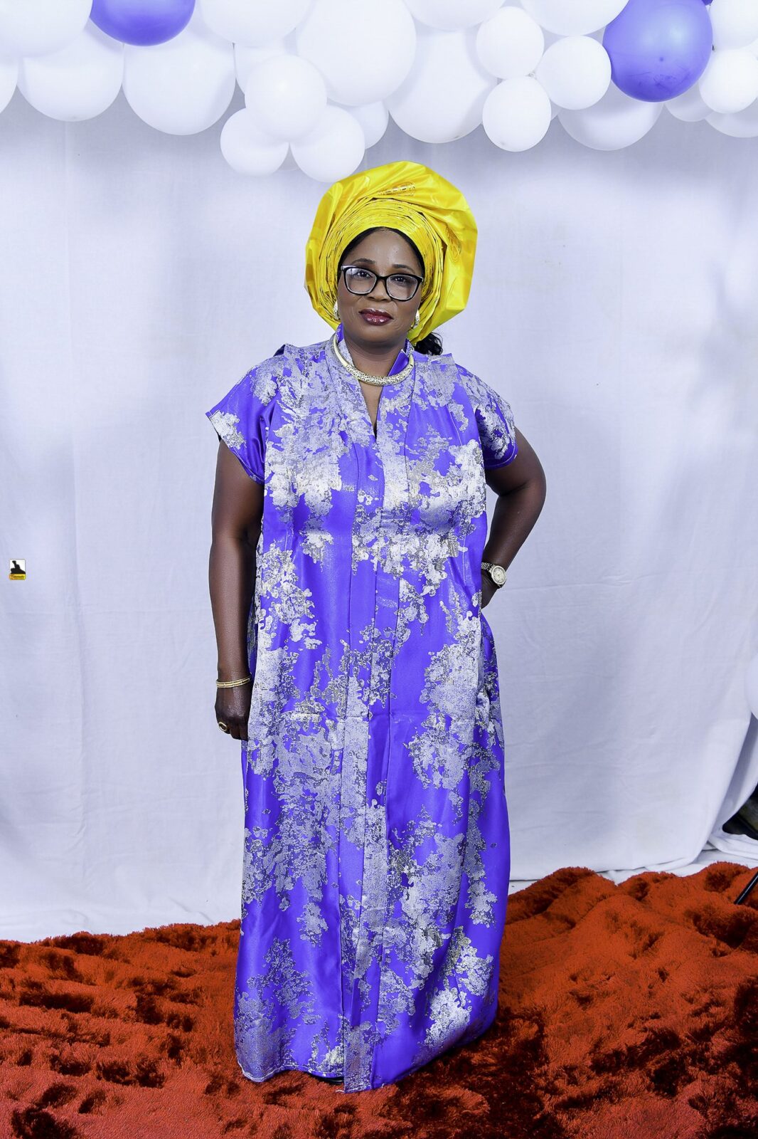 Woman in a blue patterned outfit and yellow headwrap by the balloons