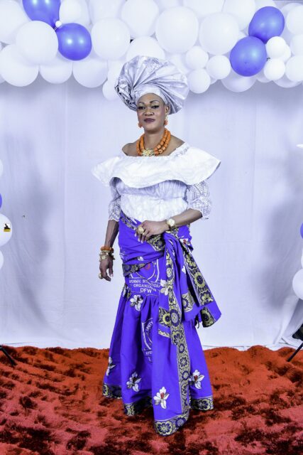 Woman in a white blouse, blue wrapper and silver headwrap by the balloons