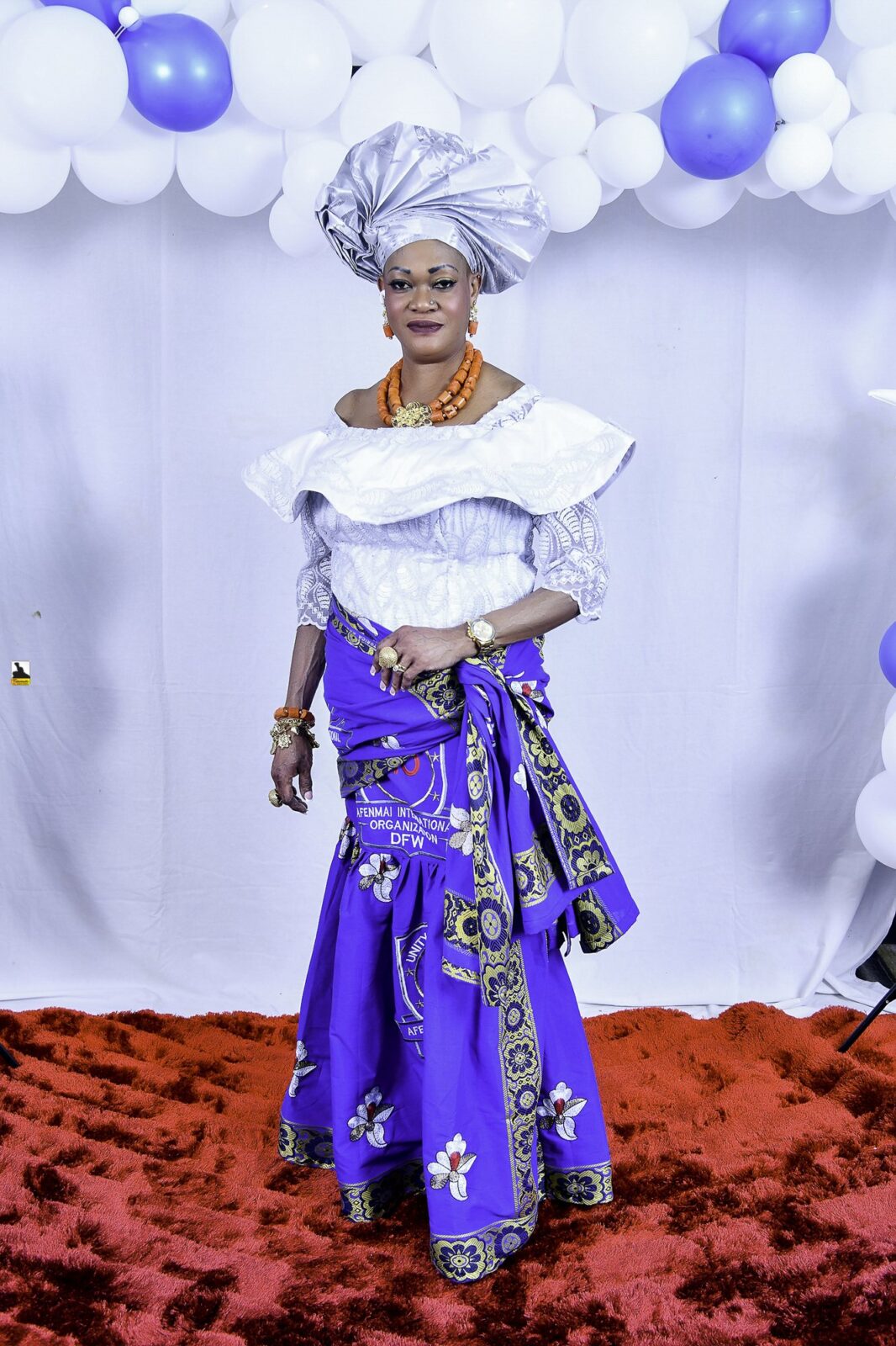 Woman in a white blouse, blue wrapper and silver headwrap by the balloons