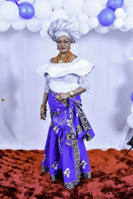 Woman in a white blouse, blue wrapper and silver headwrap by the balloons