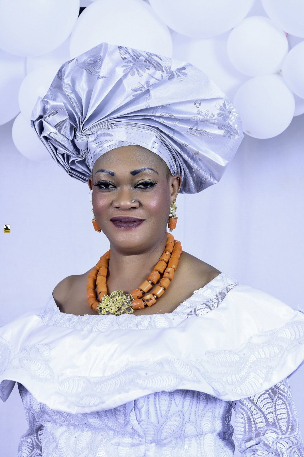 Woman in a white blouse, blue wrapper and silver headwrap by the balloons